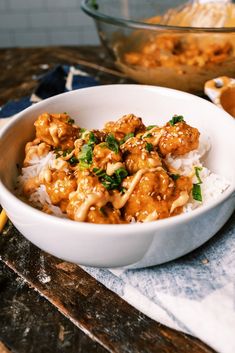 a white bowl filled with rice covered in meat and sauce on top of a wooden table