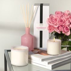 pink roses and candles sit on top of books next to a vase with reeds