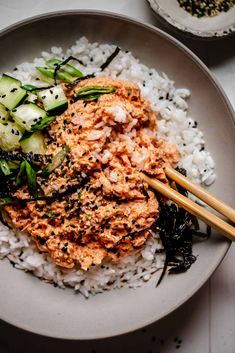 a white plate topped with rice and cucumber next to chopsticks on top of it