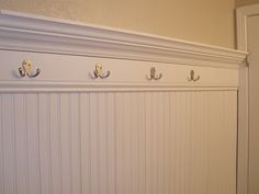 three coat hooks on the wall above a toilet in a bathroom with white paneling