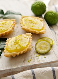 lemon tarts on a cutting board with leaves and limes in the foreground