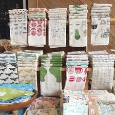 many towels are stacked on top of each other in front of a wooden table with various designs and colors