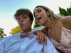 a man and woman are posing for a photo together in front of some trees with their tongue hanging out