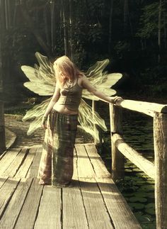 a woman with wings standing on a wooden bridge