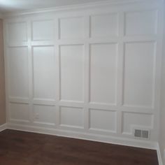 an empty room with white paneling and wood floors