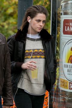 a woman is walking down the street with headphones in her ears and holding a drink