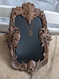 an ornate wooden frame with a necklace hanging from it's center, in front of a bed