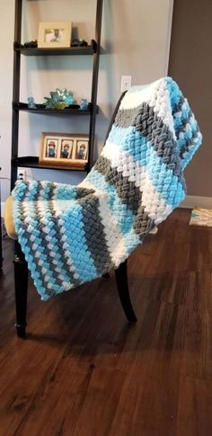 a blue and white blanket sitting on top of a wooden chair next to a book shelf