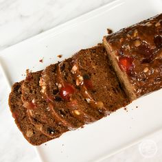 a loaf of cake on a plate with nuts and chocolate toppings, ready to be eaten