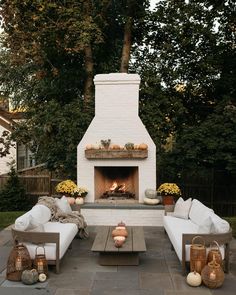 an outdoor fireplace with white couches and candles on the table in front of it