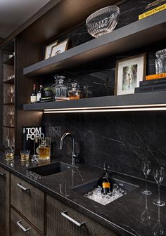 a kitchen with black marble counter tops and shelves filled with wine glasses, liquor bottles and other items