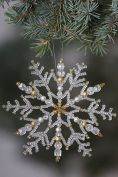 a snowflake ornament hanging from a pine tree with white and gold beads