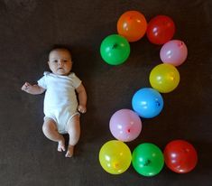 a baby laying on the floor next to some balloons that spell out the letter s