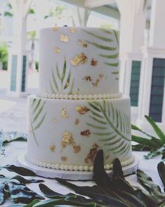 a three tiered white cake with gold leaf designs on it's sides and green leaves around the edges