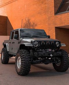 a black jeep parked in front of a building with large tires on it's sides