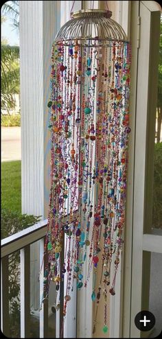 a birdcage with beads hanging from it's sides on a porch next to a window