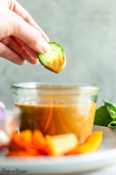 a person holding a piece of cucumber over a bowl of food on a plate