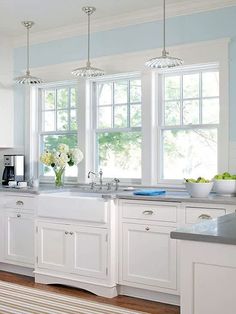 a kitchen filled with lots of white cabinets and counter top space next to two windows