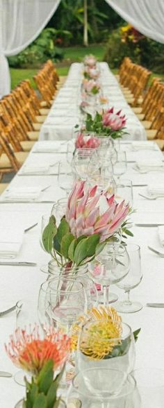 a long table is set with clear vases and flowers