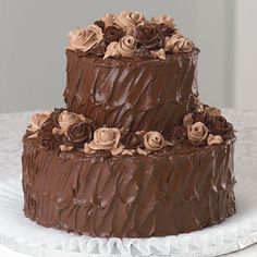 a three tier chocolate cake with roses on top sitting on a white tableclothed cloth