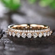 two gold wedding bands with white diamonds on them sitting on a piece of wood in front of green leaves