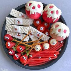 a black plate topped with apples, strawberries and cheese sticks covered in googly eyes