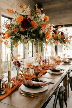 a table set with plates, candles and flowers in tall vases on top of it