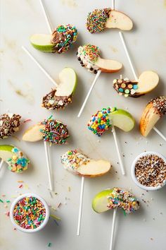 an assortment of desserts on sticks with sprinkles and apples in them