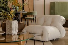 a living room with a glass coffee table and white chair next to a vase filled with flowers