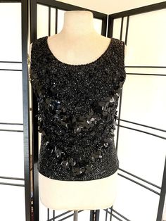 "Vintage 60s black beaded knit shell top. Please zoom in for details, photos are part of description. This lovely hand beaded top has black glass beads in a flower pattern with small black sequins and black paillettes.  It is made of 100% black wool and lined in black silk with a metal back zipper. In very good vintage condition, no holes or stains. Shown on a size six mannequin, please go by measurements provided. Measurements taken with garment lying flat  Bust: 18\" underarm to underarm ( 36\ Black Sequined Tops For Evening, Black Beaded Top For Night Out, Elegant Beaded Black Tops, Elegant Black Beaded Top, Vintage Beaded Tops For Party, Vintage Beaded Top For Night Out, Glamorous Black Beaded Tops, Vintage Beaded Sleeveless Top, Bead Knit