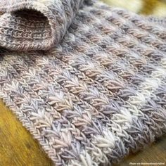 a gray and white knitted blanket laying on top of a wooden table