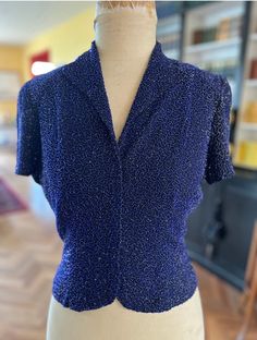 "A spectacular evening blouse/jscket made of wool crepe entirely covered in deep blue beading in a swirl pattern.  Few of these blouses survive intact but this one is in fine fine condition. Shirt sleeves, lapel collar and hooks and eye centre front closure. The pin tucks at the lower back are beautifully finished with the beads having been removed to highlight the tucks. In excellent condition  Size S-M Bust 34\" Waist 28\" Length 18\" Sleeve length 7\"" Blue Fitted Blouse For Evening, Elegant Formal Blouse With Beaded Details, Elegant Beaded Blouse For Formal Occasions, Elegant Fitted Beaded Blouse, Elegant Beaded Tops For Formal Occasions, Glamorous Fitted Beaded Blouse, Vintage V-neck Blouse For Evening, Elegant Blue Sequined Tops, Vintage Fitted Beaded Tops