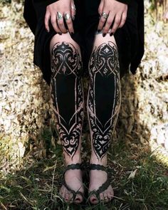 a woman with tattoos on her legs sitting in the grass