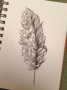 a drawing of a feather with flowers on the side and leaves in the middle, sitting on top of a notebook