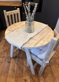 a vase with flowers sitting on top of a wooden table next to two white chairs