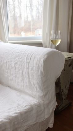 a white couch sitting next to a window with a glass of wine on top of it