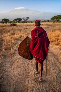 a person walking down a dirt road with a wooden shield on his back and a mountain in the background