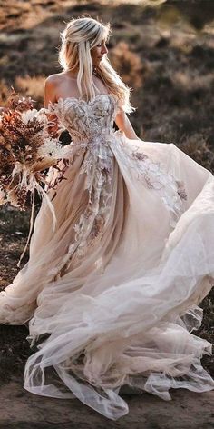 a woman in a wedding dress is walking through the woods with her bouquet on her hand