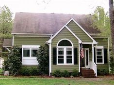 a green house with white trim and two windows on the second floor, in front of some trees