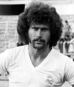 a man with an afro standing in front of a soccer field and looking at the camera