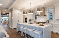 a large kitchen with white cabinets and counter tops, along with bar stools that match the hardwood flooring