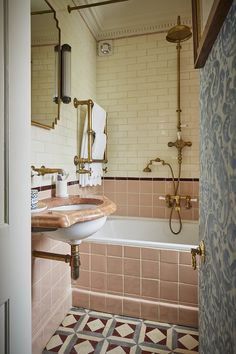 a bathroom with pink tiles and gold fixtures on the walls, along with a bathtub