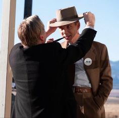 two men in suits and hats standing next to each other, one adjusting the hat on another man's head