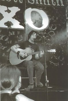 a man sitting on top of a chair playing a guitar in front of a microphone