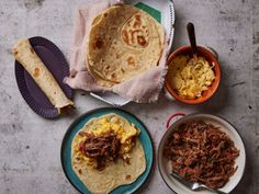 three plates filled with different types of food on top of a cement surface next to bowls and utensils