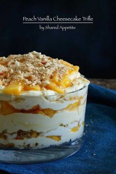 peach vanilla cheesecake trifle in a glass dish on a blue cloth with the words peach vanilla cheesecake trifle above it