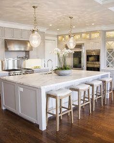 a large kitchen with white cabinets and marble counter tops, an island with four stools