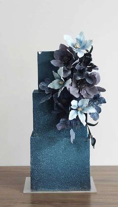 a blue cake with flowers on it sitting on top of a wooden table in front of a white wall