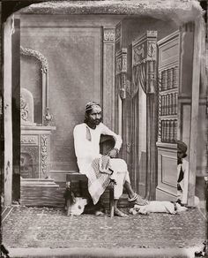 an old black and white photo of a man sitting on a chair with two dogs