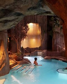 a woman in a pool with waterfall and water fall behind her, surrounded by large rocks